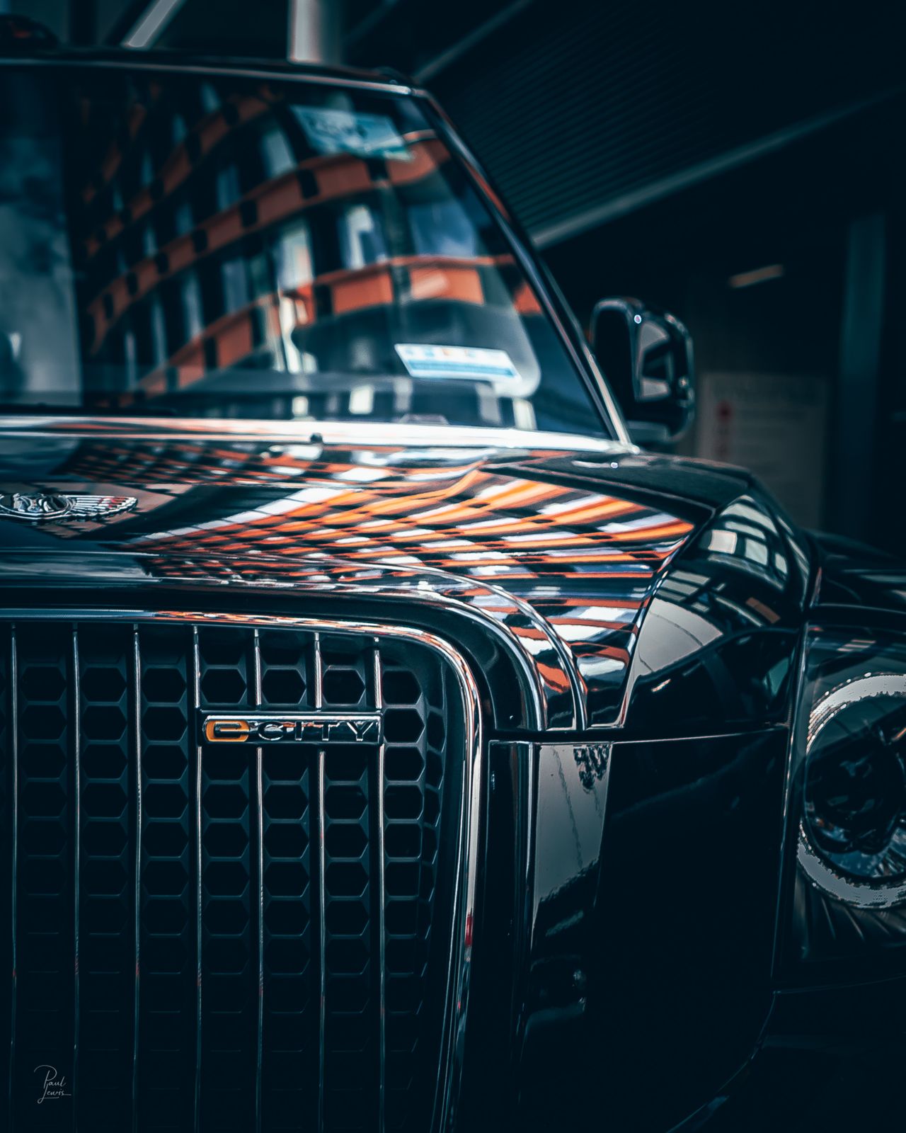 The front of a black cab, with orange reflections across its bonnet